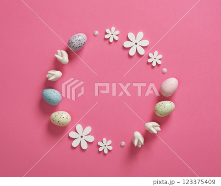 Minimalist Easter frame with white bunnies, colored eggs and wooden flowers on pink background. Space for your text. 123375409