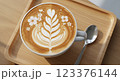 op-down view of a latte with intricate spring flower latte art, served on a wooden tray with a spoon, soft natural lighting, ultra-realistic, high resolution, close-up shot 123376144