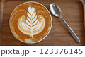 op-down view of a latte with intricate spring flower latte art, served on a wooden tray with a spoon, soft natural lighting, ultra-realistic, high resolution, close-up shot 123376145