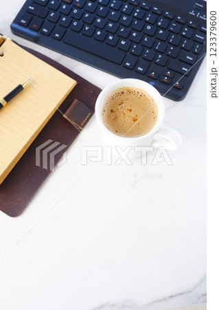 リング式のシステム手帳を広げ、コーヒー（カフェ・ラテ）を飲みながらパソコンでデスクワーク中のイメージ 123379600