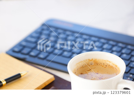 リング式のシステム手帳を広げ、コーヒー（カフェ・ラテ）を飲みながらパソコンでデスクワーク中のイメージ 123379601