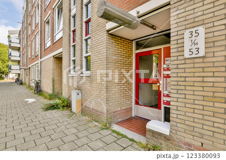 A contemporary building entrance featuring a vibrant red door and minimalist design, set along a cobblestone path with subtle greenery. A contemporary building entrance featuring a vibrant red door and minimalist design, set along a cobblestone path with subtle greenery. 123380093