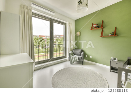 A stylish nursery featuring a green accent wall, a cozy armchair, and large windows offering plenty of natural light, creating a serene atmosphere for a child's room. 123380118