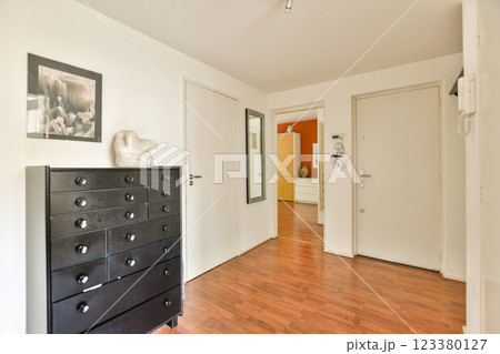 A sleek entrance hall showcasing dark wooden flooring, minimalist decor, and subtle elegance. The space features a black dresser and framed art, creating a welcoming atmosphere. A sleek entrance hall showcasing dark wooden flooring, minimalist decor, and subtle elegance. The space features a black dresser and framed art, creating a welcoming atmosphere. 123380127