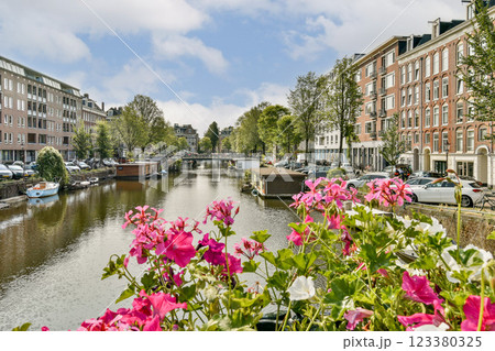 A vibrant canal scene featuring blooming flowers in the foreground, surrounded by charming buildings and greenery along the waterway. A vibrant canal scene featuring blooming flowers in the foreground, surrounded by charming buildings and greenery along the waterway. 123380325