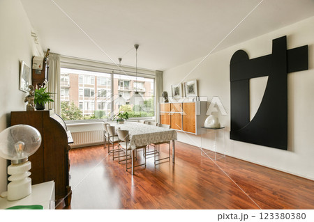 A stylish dining room featuring a wooden table, elegant chairs, and modern art pieces. Natural light floods the space, accentuating its contemporary design. A stylish dining room featuring a wooden table, elegant chairs, and modern art pieces. Natural light floods the space, accentuating its contemporary design. 123380380