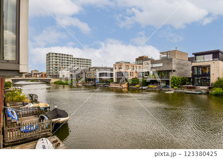 Stylish modern homes line a serene riverbank, showcasing contemporary architecture amidst lush greenery and blue skies. 123380425