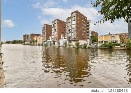 A picturesque view of a modern urban complex along a tranquil waterfront, reflecting the buildings on the water surface under a clear sky. A picturesque view of a modern urban complex along a tranquil waterfront, reflecting the buildings on the water surface under a clear sky. 123380428