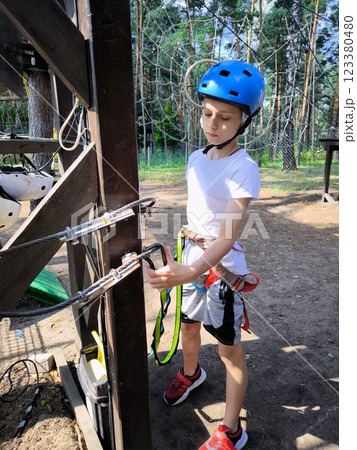 A child in a forest adventure park. A kid in a blue helmet and a white T-shirt is climbing a cable car. A children's entertainment center in an outdoor park A child in a forest adventure park. A kid in a blue helmet and a white T-shirt is climbing a cable car. A children's entertainment center in an outdoor park 123380480