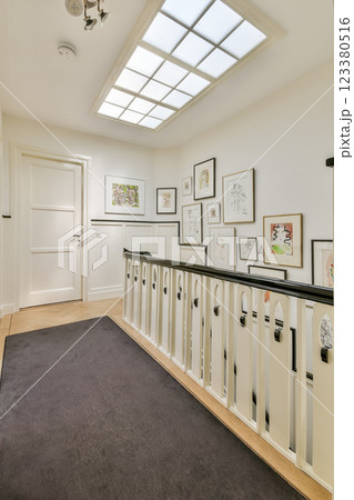 A spacious, well-lit modern hallway features a stylish railing and walls adorned with framed art, creating an inviting atmosphere. A spacious, well-lit modern hallway features a stylish railing and walls adorned with framed art, creating an inviting atmosphere. 123380516