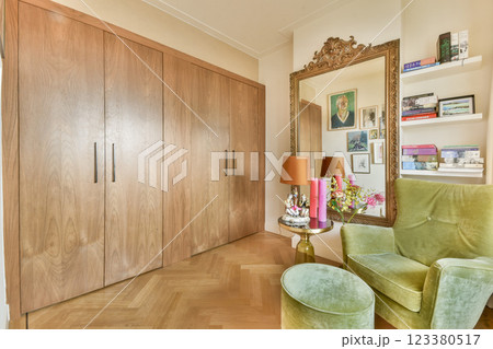 A stylish interior featuring a green armchair, wooden cabinet, and decorative mirror. The space combines comfort with modern aesthetics, highlighting rich textures and colors. A stylish interior featuring a green armchair, wooden cabinet, and decorative mirror. The space combines comfort with modern aesthetics, highlighting rich textures and colors. 123380517
