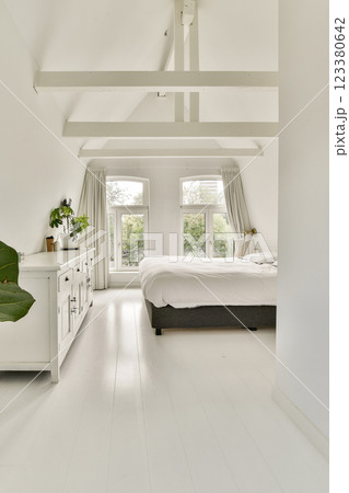 A spacious, light-filled bedroom with a minimalist design featuring white walls, large windows, and elegant furnishings that create a calm atmosphere. A spacious, light-filled bedroom with a minimalist design featuring white walls, large windows, and elegant furnishings that create a calm atmosphere. 123380642