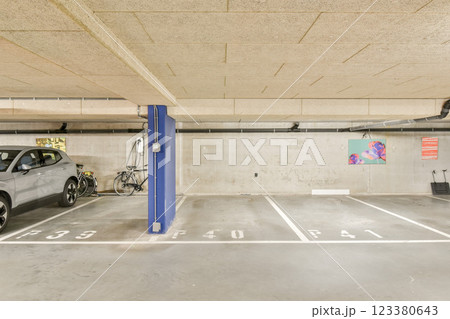 A spacious parking garage featuring cars, a bicycle, and marked parking spots, illuminated by overhead lighting, emphasizing urban architecture. 123380643