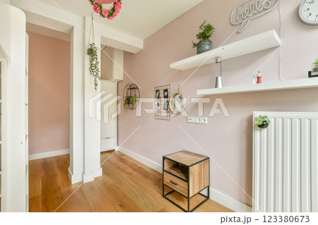 A contemporary room featuring soft pink walls, elegant shelving, wooden flooring, and greenery, showcasing a minimalist and welcoming atmosphere. 123380673