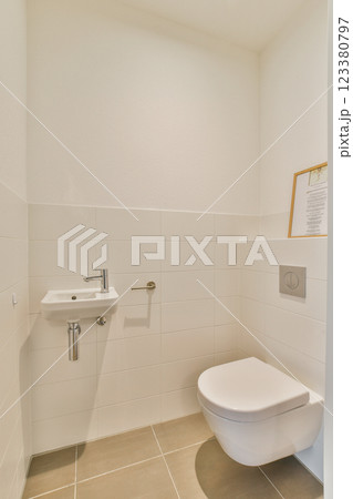 A clean and minimalistic bathroom featuring a modern toilet and sink against white tiled walls. The design emphasizes simplicity and functionality. 123380797