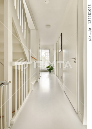 A bright and minimalist hallway featuring a stairway, white walls, and natural light. The decor is simple yet elegant, enhancing the spacious feel of the area. 123381048