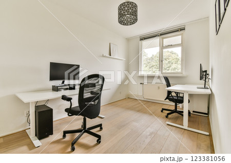 A bright and airy home office featuring two desks, modern chairs, and natural light entering through the window, promoting a productive atmosphere. 123381056