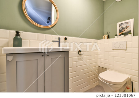 Elegant bathroom featuring a minimalist design with a round mirror, soft green walls, and stylish fixtures, creating a serene space for relaxation. Elegant bathroom featuring a minimalist design with a round mirror, soft green walls, and stylish fixtures, creating a serene space for relaxation. 123381067