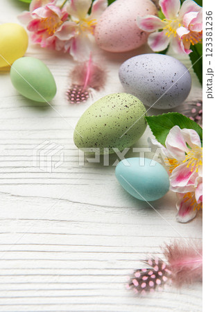 Colorful easter eggs and spring flowers creating festive border on white wood 123381236