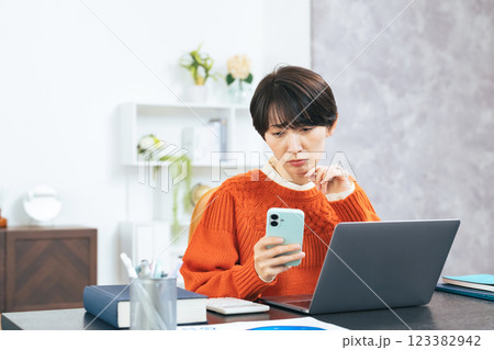 スマホとノートパソコンを見ながら悩むミドル女性 スマホとノートパソコンを見ながら悩むミドル女性 123382942