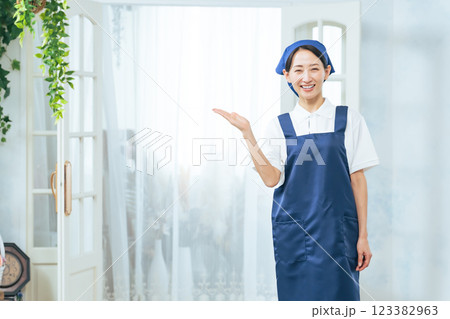 扉の前に立って案内するエプロンをつけたミドルエイジ女性 123382963