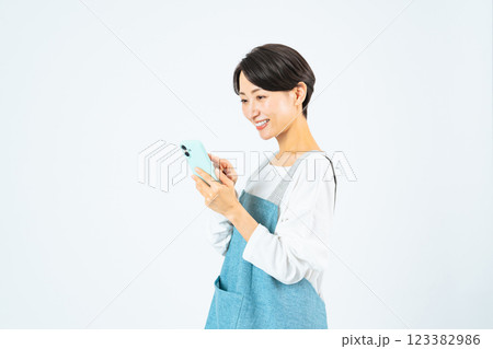 笑顔でスマホを使うエプロンをつけたミドル女性 123382986