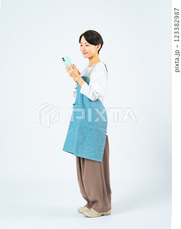 スマホを使うエプロンをつけたミドル女性の全身写真 123382987