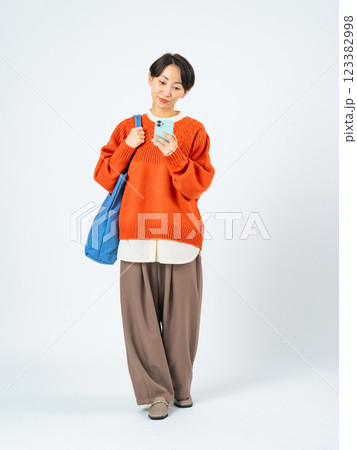スマホを持って歩くおしゃれなミドル女性の全身写真 123382998