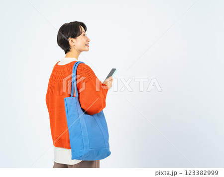 スマホを持って歩くおしゃれなミドル女性の後ろ姿 123382999