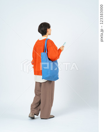 スマホを持って歩くおしゃれなミドル女性の後ろ姿の全身写真 123383000