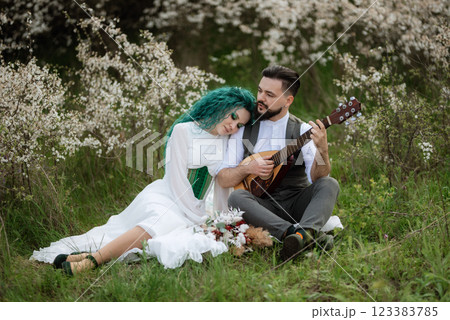 a bearded groom plays a stringed instrument and a girl sits in a spring meadow a bearded groom plays a stringed instrument and a girl sits in a spring meadow 123383785