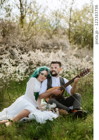 a bearded groom plays a stringed instrument and a girl sits in a spring meadow a bearded groom plays a stringed instrument and a girl sits in a spring meadow 123383786