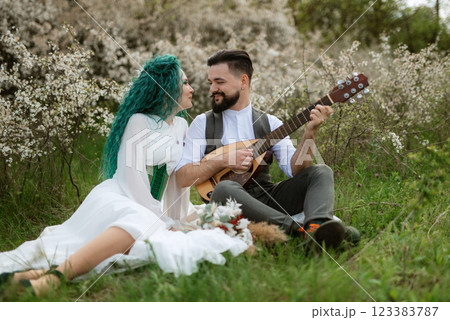 a bearded groom plays a stringed instrument and a girl sits in a spring meadow a bearded groom plays a stringed instrument and a girl sits in a spring meadow 123383787