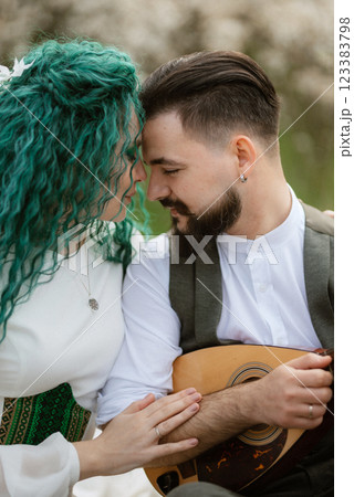 a bearded groom plays a stringed instrument and a girl sits in a spring meadow a bearded groom plays a stringed instrument and a girl sits in a spring meadow 123383798