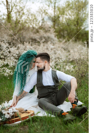 a bearded groom plays a stringed instrument and a girl sits in a spring meadow a bearded groom plays a stringed instrument and a girl sits in a spring meadow 123383810