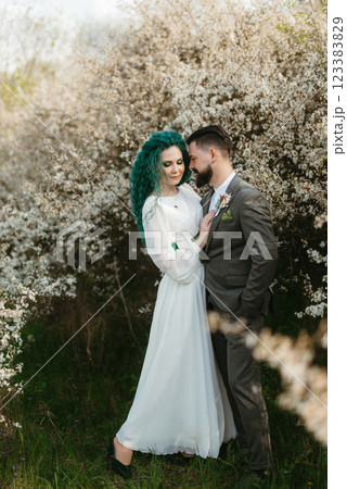 a bearded groom plays and a girl with green hair against the background of blooming spring 123383829