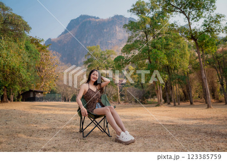 Portrait of sexy asian woman in a military print strapless dress sitting on a lawn chair camping in the woods. 123385759