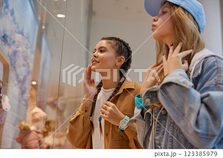 Happy teenage girls friends looking through showcase window in shopping mall Happy teenage girls friends looking through showcase window in shopping mall 123385979