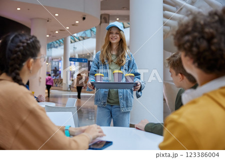 Girl carrying tray with coffee for friends relaxed in shopping mall cafeteria 123386004