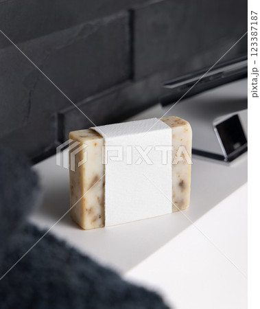 Beige soap with blank label on washbasin near faucet and dark grey bath towel close up, mockup 123387187