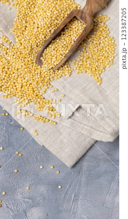 Raw uncooked yellow millet grain in a wooden spoon on grey table, top view. Ancient food Raw uncooked yellow millet grain in a wooden spoon on grey table, top view. Ancient food 123387205