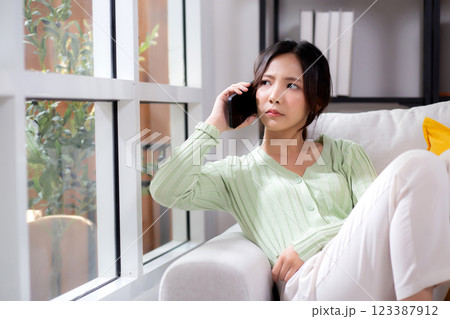 Asian young woman stress and worried sitting on sofa while speaking on smart phone in living room. Asian young woman stress and worried sitting on sofa while speaking on smart phone in living room. 123387912