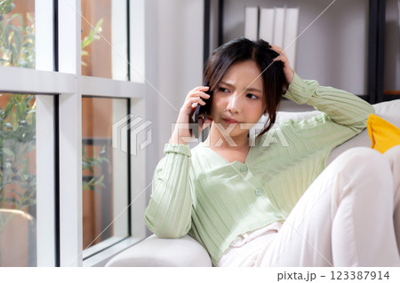 Asian young woman stress and worried sitting on sofa while speaking on smart phone in living room. Asian young woman stress and worried sitting on sofa while speaking on smart phone in living room. 123387914