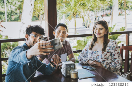 Young friends taking a selfie in a coffee shop. Three happy people in a coffee shop taking a selfie. Front view of teenage friends taking selfie and having fun in a cafe restaurant Young friends taking a selfie in a coffee shop. Three happy people in a coffee shop taking a selfie. Front view of teenage friends taking selfie and having fun in a cafe restaurant 123388212