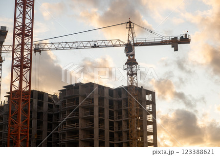 Cranes are lifting materials at a busy construction site as the sun sets, casting a warm glow over the ongoing building project. 123388621