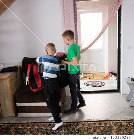 Two young boys get ready for school, packing their backpacks near the doorway of their home, preparing for the day ahead. Two young boys get ready for school, packing their backpacks near the doorway of their home, preparing for the day ahead. 123389258