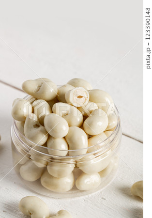 Cashew nuts in milk chocolate. Glass jar on a white wooden background. 123390148