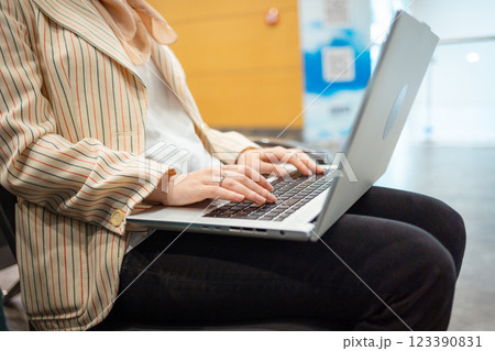 Mid shot of Caucasian elegant young woman is sitting on chair in waiting room of airport and working on laptop. Concept of remote work and travel 123390831