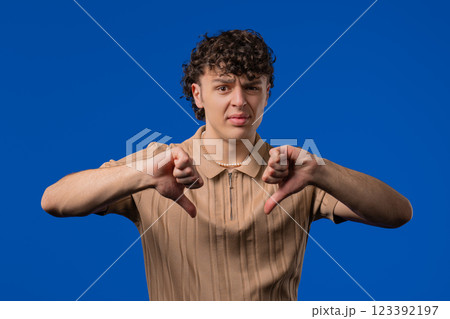 Young curly haired man with sign of dislike. Guy shaming, expressing thumbs-down Young curly haired man with sign of dislike. Guy shaming, expressing thumbs-down 123392197