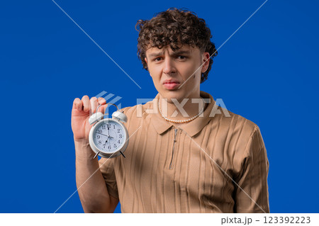 Woken Up By Alarm Clock Sleepy Handsome Man Holding It In Hand. Blue Background 123392223